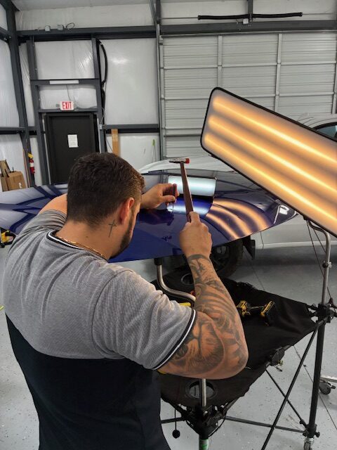 Man repairing car dent with tools.