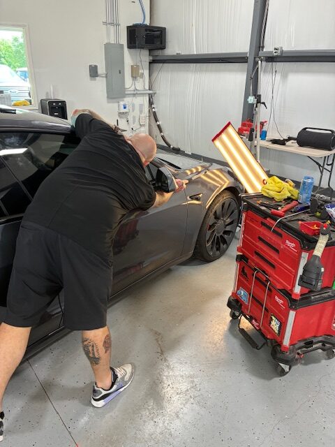Person repairing car dent in garage.